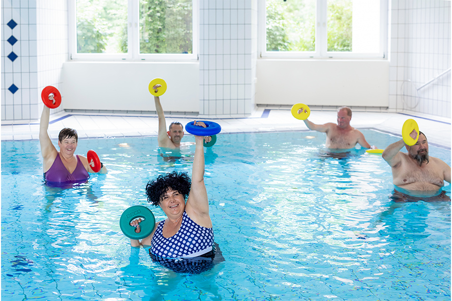 Mehrere Patienten trainieren bei der Wassergymnastik mit Gewichten.